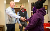 Zoom image: Philip Glick, Faculty Senate Chair, and Domenic Licata, Professional Staff Senate Chair, greeting an adopted holiday family member of the Office of Shared Governance, at the holiday party and gift distribution in Allen Hall. 