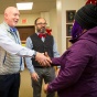 Zoom image: Philip Glick, Faculty Senate Chair, and Domenic Licata, Professional Staff Senate Chair, greeting an adopted holiday family member of the Office of Shared Governance, at the holiday party and gift distribution in Allen Hall. 