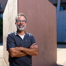Photo shows a man with gray hair and a gray beard standing outside. 