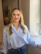 Photo shows a person smiling at the camera with blonde hair and a blue striped shirt. 
