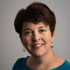 Photo of Kathleen A. Parks, smiling with a short haircut, wearing a green shirt and silver metal shiny earrings. 