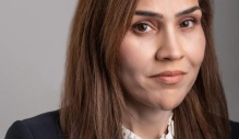 Photo shows a woman with brown hair wearing a black blazer. 
