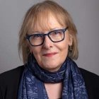 Photo shows a person in blue glasses smiling at the camera. 