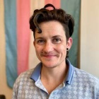 Photo shows a person smiling at the camera. They have dark hair and a blu collared shirt. 