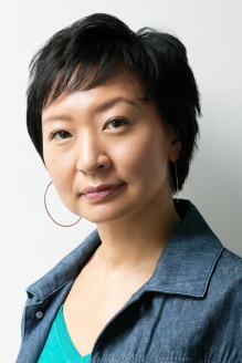 Picture of Cathy Park Hong, wearing a green sweater and dark blue denim jacket. 
