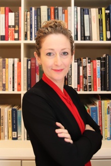 Photo of Cassidy Sugimoto, Woman wearing a red shirt and black blazer in front of a bookcase. 
