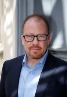 Image of a man in a blue suit coat and glasses. 