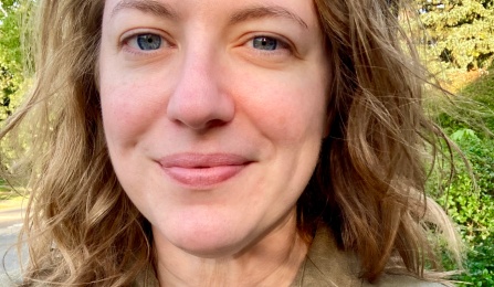 Photo of a person with wavy hair, wearing a green shirt, outdoors. 
