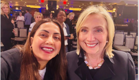 Senay Imre (left), wearing black blazer with long center partitioned hair and smiling with Hilary Clinton (right), wearing black blzer, blonde hair smiling at the camera. 