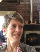 Prof. Carine M Mardorossian has short hair, is looking to their left and smililing and the background is a wood burning stove. 