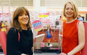 Two women posing with a Barbie, smiling at the camera. 