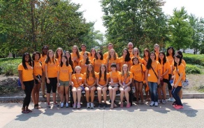 Photo is taken of a group of people in orange t shirts, standing outdoors. 