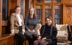 Three people in a library, smiling at the camera. 