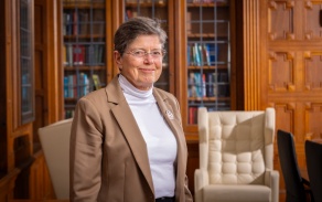 Photo shows a woman with glasses, smiling at the camera. 