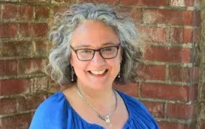 Photo shows a woman with glasses, smiling at the camera. 