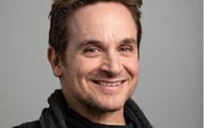 Photo shows a man with short hair, smiling at the camera. 