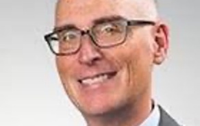 photo of a man in a suit with glasses, smiling at the camera. 