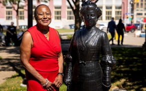 Woman in red dress stands outdoors with a statue. 