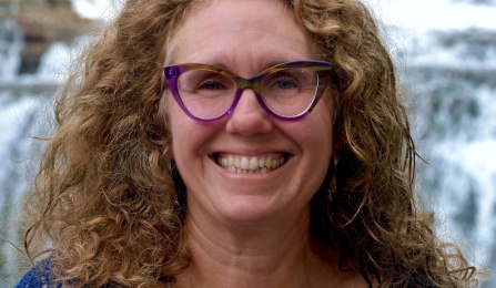 Photo shows a woman with curly hair smiling at the camera. 