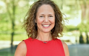 A woman with brown hair, wearing a red sleeveless shirt, smiling at the camera. 