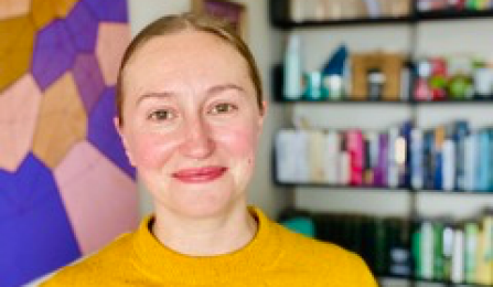 A woman with dark blonde hair, wearing a yellow shirt, smiling at the camera. 