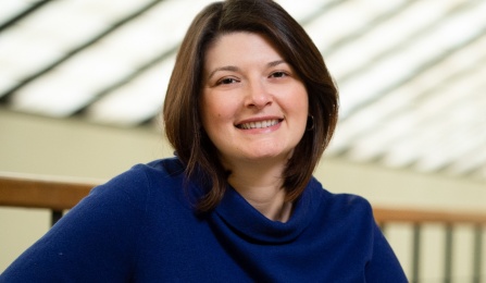 A woman with dark brown hair, wearing a blue shirt, smiling at the camera. 