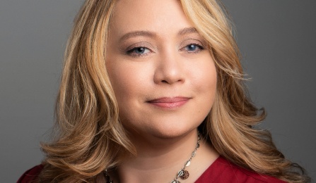 A woman with dark blonde hair, wearing a red shirt, smiling at the camera. 