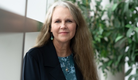 A woman with brown hair, wearing a blue shirt, smiling at the camera. 