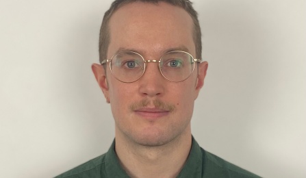 A man in a green shirt, wearing glasses, looking at the camera. 