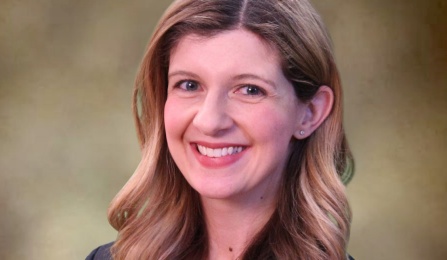 A woman with dark blonde hair, wearing a black blazer, smiling at the camera. 