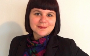 Photo shows one woman smiling at the camera. She is wearing a black blazer and has dark hair. 