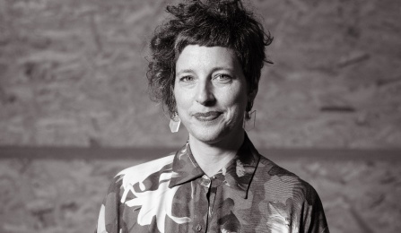 Photo shows a woman in a black and white photo with short hair, looking at the camera. 