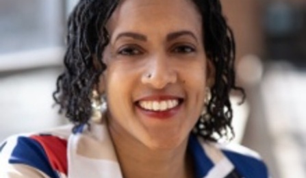 A woman with dark brown hair, wearing a blazer, smiling at the camera. 