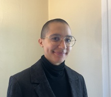 Person wearing a black shirt and jacket, smiling at the camera. 