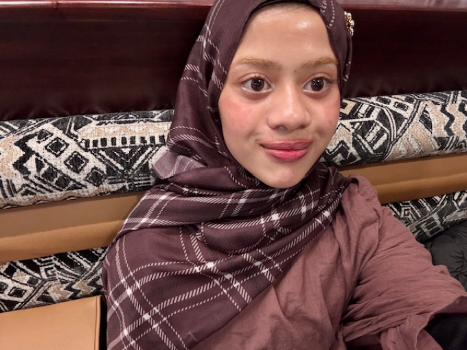 Person with a purple plaid scarf, smiling to the right of the camera. 