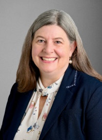 Photo shows woman wearing a blue blazer looking at the camera. 