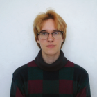 Image of Devin Gaichas, who has short, bleached hair, wearing a turtleneck sweater with a green, red, and black checkerboard pattern. 