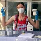 Image of Valerie Skakun, who has long, braided hear, wearing gloves, a mask, and a red tank top, holding her SCOBY. 