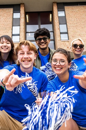 A group of UB supportings putting their horns up dressed in UB blue. 