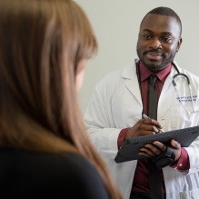 A doctor is asking a patient questions and putting answers on a digital tablet. 
