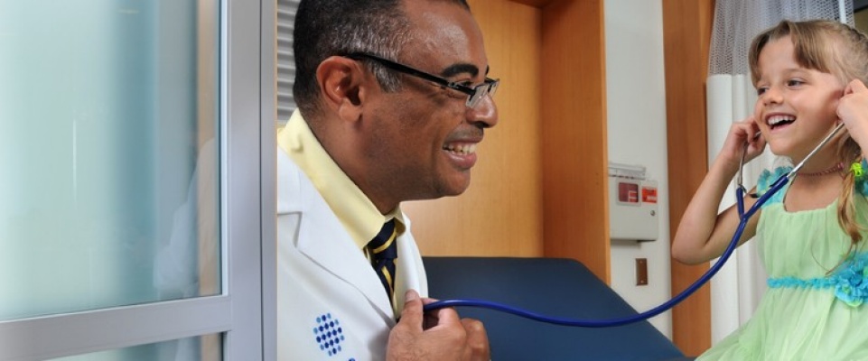 UBMD doctor with a pediatric patient, allowing her to use his stethescope and listen to his heart. 