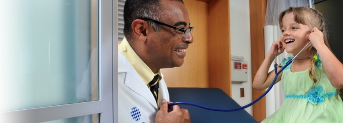 UBMD doctor with a pediatric patient, allowing her to use his stethescope and listen to his heart. 