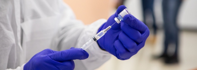 Person wearing gloves preparing a vaccine syringe. 