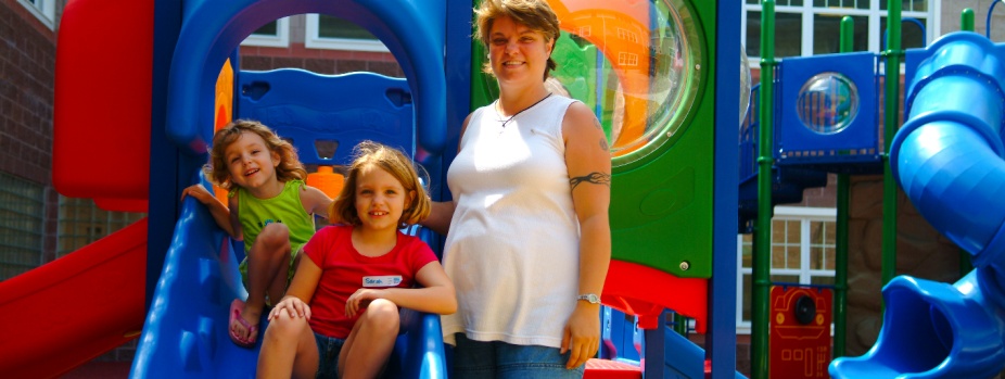 smiling woman with two young children at a colorful playground play structure. 
