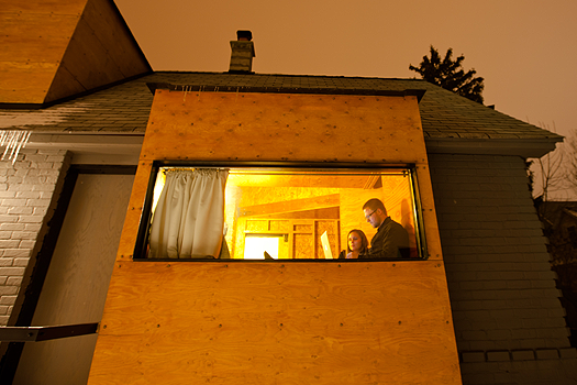 a young man and his girlfriend as seen through a long, rectangular window in a small brick house