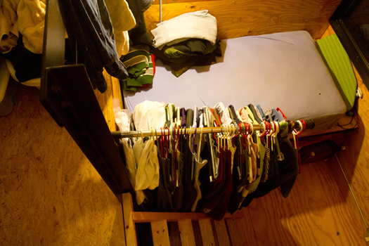 clothes hanging next to a bed in a small, wooden room