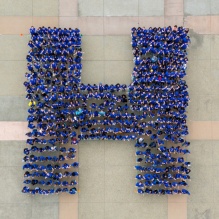 overhead view of students in blue shirts forming a capital H. 