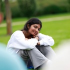 student smiling and sitting outside with arms on knees and head resting on arm. 