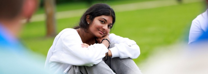 student smiling and sitting outside with arms on knees and head resting on arm. 