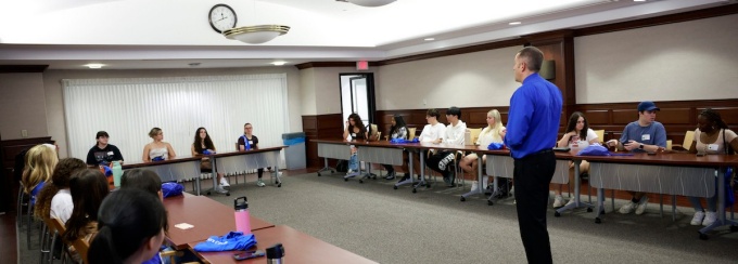 tim matthews teaching a class in a big room with desks in a horseshoe shape. 